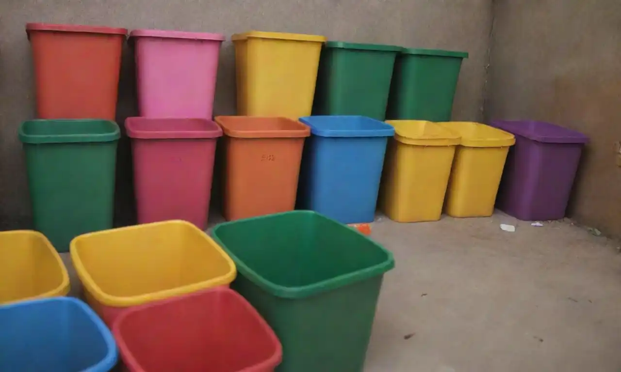 Bins de colores llenos de materiales reciclables ordenados junto con un proyecto de arte creativo hecho de residuos.
